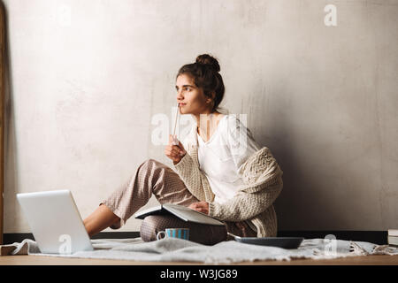 Foto der fokussierten Woman tragen Freizeitkleidung schreiben in Tagebuch und mit Laptop, während auf dem Boden zu Hause sitzen Stockfoto