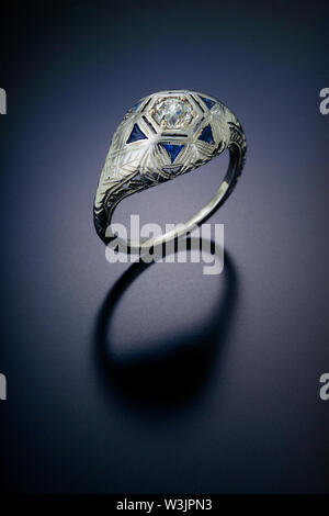 Eine geometrische Dome Stil antike Diamond Engagement Ring mit einem carat Zentrum Stein und die von Akzent Dreieck schneiden Saphire in Platin umgeben. Stockfoto