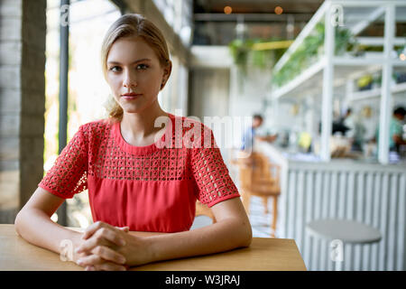 Lifestyle Portrait von selbstbewussten jungen trendigen tausendjährigen Geschäftsfrau mit blonden Haaren sitzen an den hölzernen Tisch in hellen und modernen Restaurant Stockfoto