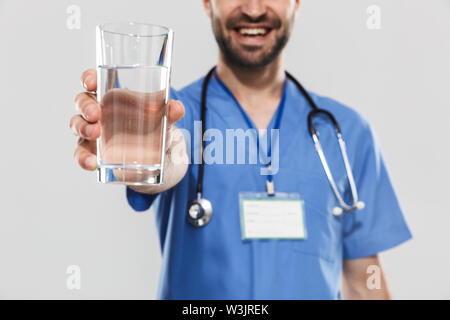 Nahaufnahme eines attraktiven jungen fröhlichen männlicher Arzt tragen unifrom auf weißem Hintergrund, das Glas Wasser Stockfoto
