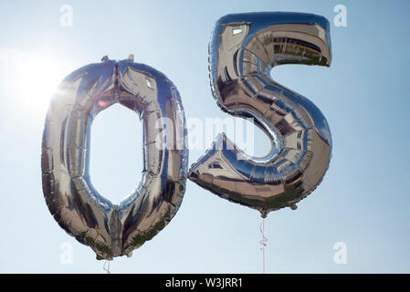 Die Nummern 0 und 5 silber Helium gefüllte Ballone gegen einen blauen Himmel mit Sonnenschein Stockfoto