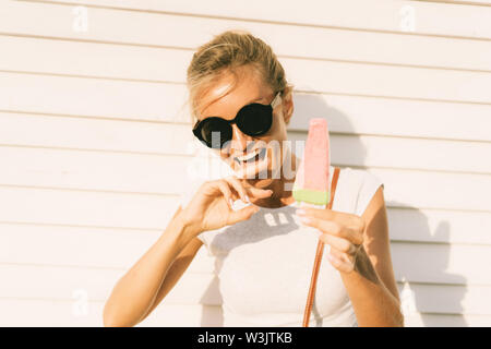 Das Mädchen leckt ihre Finger schmutzig Popsicle aufgetaut. Fröhlich und heiter Emotionen, Sommerferien und heissen Sommer. Gefrorene desser schmilzt schnell in der Stockfoto