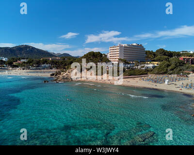 Antenne Wasserseite Blick auf das türkisfarbene Meer felsige Küstenlinie von Paguera oder Peguera Strand mit Liegen und Sonnenschirmen in der südwestlichen Ecke von Mallorca, Spanien