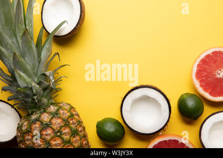 Blick von oben auf die ganze reife Ananas, Zitrusfrüchte und Kokosnuss Hälften auf gelbem Hintergrund Stockfoto