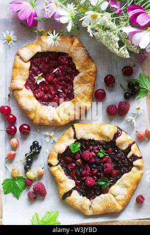 Galette Torten mit saftigen Beeren füllen, Beeren und wilde Blumen auf einem hölzernen Hintergrund. Rustikaler Stil, selektiven Fokus. Stockfoto