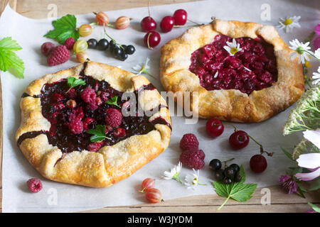 Galette Torten mit saftigen Beeren füllen, Beeren und wilde Blumen auf einem hölzernen Hintergrund. Rustikaler Stil, selektiven Fokus. Stockfoto