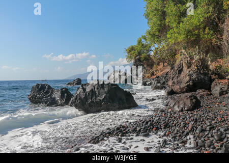 Steiniger Strand mit schwarzem Lavastrand Kieselsteinen. Rocky bizarre Formationen, die sich über der Oberfläche des Ozeans. Sea Surf Breaks auf Klippen und die Küste. Meerwasser Stockfoto