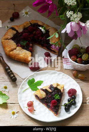 Süße Torte Galette mit saftigen Beeren füllen, Beeren und wilde Blumen auf einem hölzernen Hintergrund. Rustikaler Stil, selektiven Fokus. Stockfoto