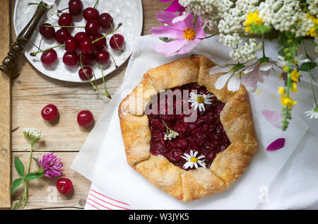 Süße Torte Galette mit saftigen Beeren füllen, Beeren und wilde Blumen auf einem hölzernen Hintergrund. Rustikaler Stil, selektiven Fokus. Stockfoto