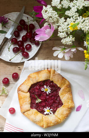 Süße Torte Galette mit saftigen Beeren füllen, Beeren und wilde Blumen auf einem hölzernen Hintergrund. Rustikaler Stil, selektiven Fokus. Stockfoto