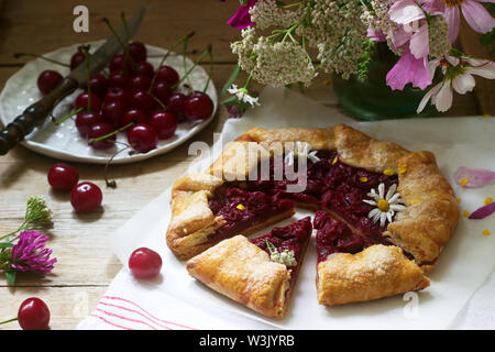 Süße Torte Galette mit saftigen Beeren füllen, Beeren und wilde Blumen auf einem hölzernen Hintergrund. Rustikaler Stil, selektiven Fokus. Stockfoto