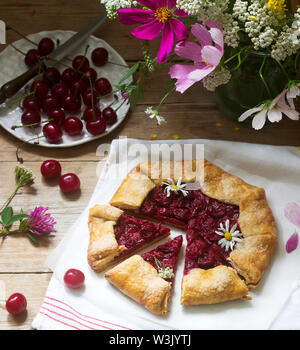 Süße Torte Galette mit saftigen Beeren füllen, Beeren und wilde Blumen auf einem hölzernen Hintergrund. Rustikaler Stil, selektiven Fokus. Stockfoto
