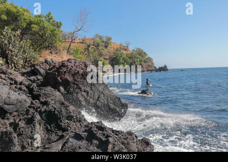 Steiniger Strand mit schwarzem Lavastrand Kieselsteinen. Rocky bizarre Formationen, die sich über der Oberfläche des Ozeans. Sea Surf Breaks auf Klippen und die Küste. Meerwasser Stockfoto