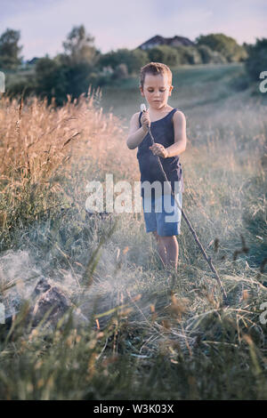 Little Boy rösten Marshmallow über einem Lagerfeuer auf einer Wiese. Ehrliche Menschen, echte Momente, in authentischen Situationen Stockfoto