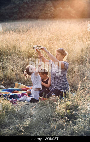 Familie Ausgabe Zeit zusammen auf einer Wiese, in der Nähe der Natur, Eltern und Kinder zusammen spielen, Coronet von wilden Blumen. Ehrliche Menschen, echte Stockfoto