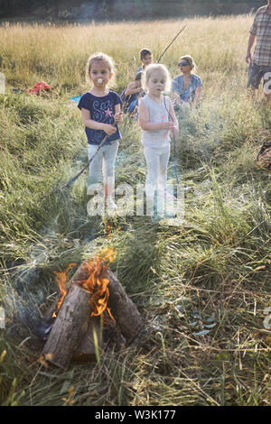 Kinder essen, nachdem sie eine Marshmallows rösten über einem Lagerfeuer auf einer Wiese. Ehrliche Menschen, echte Momente, in authentischen Situationen Stockfoto