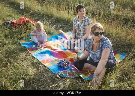 Familie Ausgabe Zeit zusammen auf einer Wiese, in der Nähe der Natur, Braten, Marshmallows über einem Lagerfeuer, Eltern und Kinder zusammen spielen und Sitzen o Stockfoto