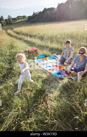 Familie Ausgabe Zeit zusammen auf einer Wiese, in der Nähe der Natur, Braten, Marshmallows über einem Lagerfeuer, die Eltern und die Kinder sitzen auf einer Decke im Gras. Stockfoto