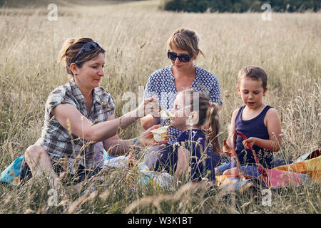 Familien und Freunde Ausgabe Zeit zusammen auf der Wiese, in der Nähe der Natur. Mütter stillen Kinder, sitzend auf einer Decke im Gras. Ehrliche Menschen, echte Mo Stockfoto