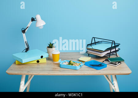 Studio shot von Arbeitsbereich mit Tisch und Lunchpaket auf blauem Hintergrund Stockfoto