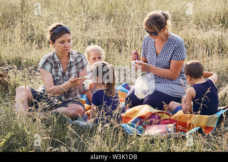 Familien und Freunde Ausgabe Zeit zusammen auf der Wiese, in der Nähe der Natur. Mütter stillen Kinder, sitzend auf einer Decke im Gras. Ehrliche Menschen, echte Mo Stockfoto