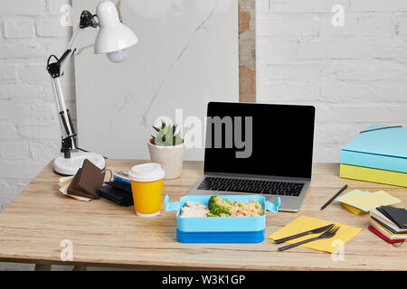 Lunch Box mit Reis, Huhn und Brokkoli am Arbeitsplatz mit Laptop auf Holztisch auf weißem Hintergrund, illustrative Editorial Stockfoto