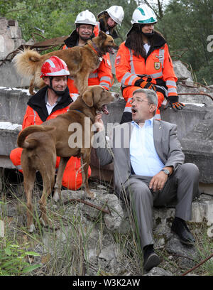 Neubrandenburg, Deutschland. 16. Juli, 2019. Bei seinem Besuch in der Malchiner Rescue Dog Squadron, Lorenz Caffier (CDU), Innenminister der Zustand von Malchin, sitzt mit den Mitgliedern auf einem Haufen Schutt in einem Bereich Schulungen, neben ihm der Portugiesischen Schäferhund 'Otto'. Während der Demonstration einer Suche in den Ruinen eines ehemaligen Kraftwerks, wurde er von den Fähigkeiten der Suche Hunde überzeugt. Das Relais team, 2003 gegründet, hat derzeit 22 Ehrenmitglieder mit 10 Hunden. Quelle: Bernd Wüstneck/dpa-Zentralbild/dpa/Alamy leben Nachrichten Stockfoto