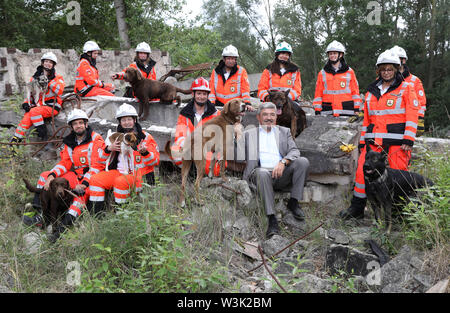 Neubrandenburg, Deutschland. 16. Juli, 2019. Bei seinem Besuch in der Malchiner Rescue Dog Squadron, Lorenz Caffier (CDU), Innenminister der Zustand von Malchin, sitzt mit den Mitgliedern auf einem Haufen Schutt in einem Bereich Schulungen, neben ihm der Portugiesischen Schäferhund 'Otto'. Während der Demonstration einer Suche in den Ruinen eines ehemaligen Kraftwerks, wurde er von den Fähigkeiten der Suche Hunde überzeugt. Das Relais team, 2003 gegründet, hat derzeit 22 Ehrenmitglieder mit 10 Hunden. Quelle: Bernd Wüstneck/dpa-Zentralbild/dpa/Alamy leben Nachrichten Stockfoto