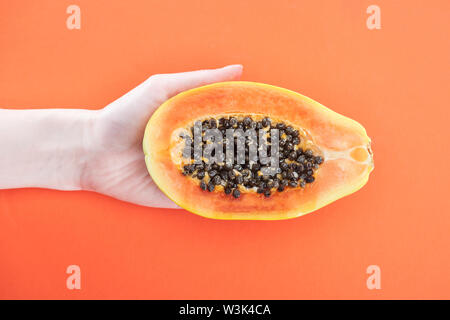 7/8-Ansicht von Frau mit reifer exotischer papaya Hälfte mit schwarzen Samen isoliert auf Orange Stockfoto