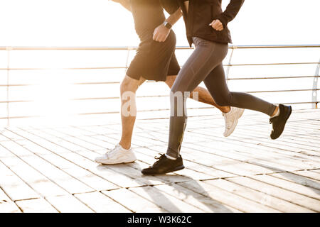 Zugeschnittenes Bild Seitenansicht eines sportlichen jungen Fitness paar Sportbekleidung jogging zusammen tragen am Strand Stockfoto