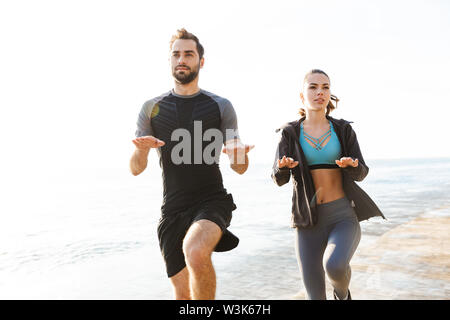 Foto von Konzentriertem starke zwei junge Sport Frau und Mann Freunde Liebespaar am Strand in der Nähe des Meer Übungen für die Beine springen. Stockfoto