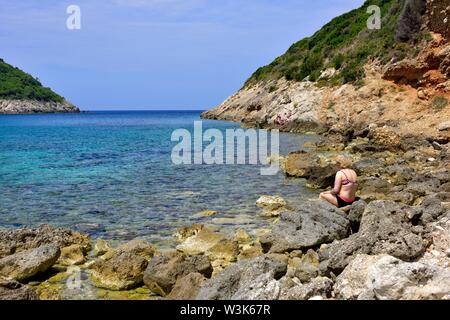 Eine Frau sitzt auf ein paar Felsen, Porto timoni, Kap Arillas und Afionas, Korfu, Griechenland, Ionische Inseln Stockfoto