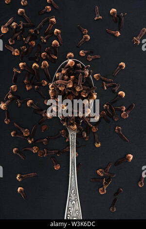 Blick von oben auf die nelke Samen in silbernen Löffel auf schwarzem Hintergrund Stockfoto