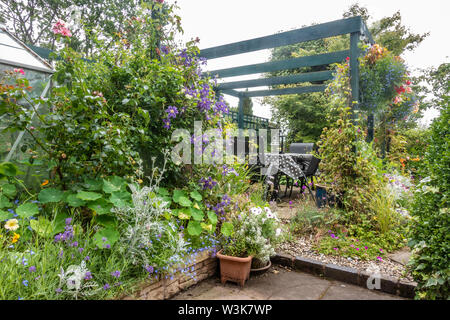 Tisch und Stühle unter eine hölzerne Pergola in einem Bauerngarten. Stockfoto