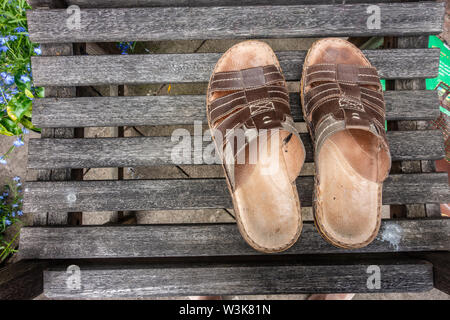 Ein paar Sandalen aus Leder für Männer auf einer hölzernen Sitz in einem Garten. Stockfoto