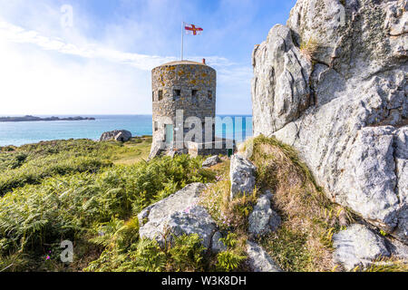 Die Guernsey-Flagge über Loophole Tower No 5 L'Ancresse (Nid de l'Herbe, Vale), Guernsey, Channel Islands UK - erbaut um 1778 - 79. Stockfoto