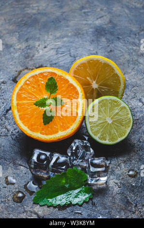 Scheiben von Orange, Zitrone und Limette mit Minze auf einen konkreten Hintergrund mit Stücken Eis. Stockfoto