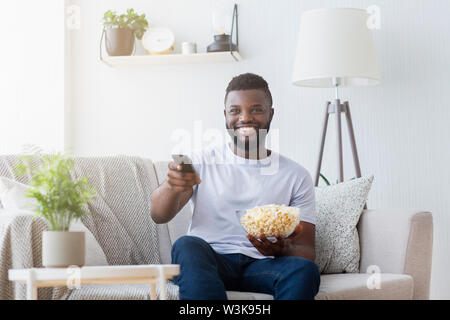 Mann hält TV-Fernbedienung und Popcorn in der Hand Stockfoto