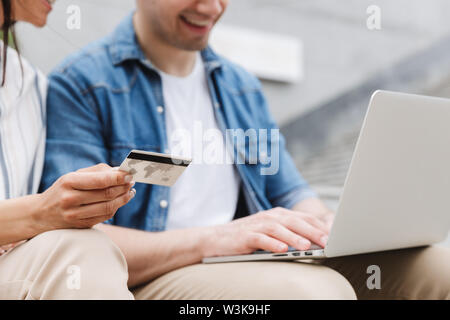 Zugeschnittenes Bild der glücklichen jungen erstaunliche paar Geschäftsleute Kollegen draußen außerhalb mit Laptop Computer mit Kreditkarte. Stockfoto