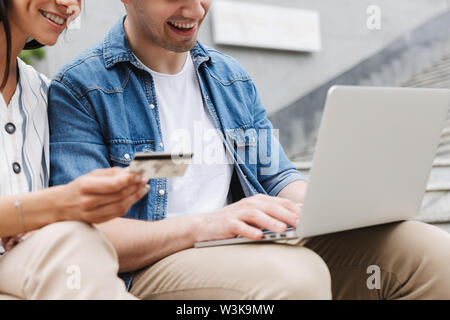Zugeschnittenes Bild der glücklichen jungen erstaunliche paar Geschäftsleute Kollegen draußen außerhalb mit Laptop Computer mit Kreditkarte. Stockfoto