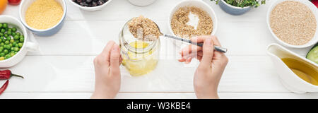 7/8-Ansicht von Frau hinzufügen Couscous in Glas mit Öl auf Holz- weißer Tisch, Panorama-Aufnahme ein. Stockfoto