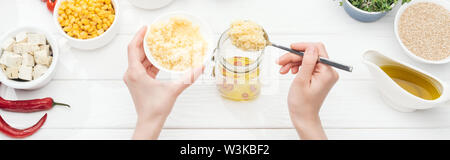 Teilweise mit Blick auf die Frau, die das Hinzufügen von Couscous, Glas auf Holz weiß Tisch, Panorama-Aufnahme ein. Stockfoto