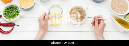 Teilweise mit Blick auf die Frau hinzufügen Couscous in Glas mit Öl auf Holz- weißer Tisch, Panorama-Aufnahme ein. Stockfoto