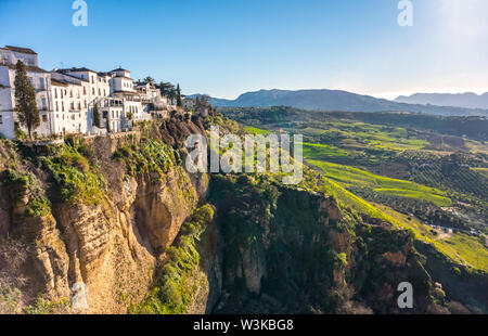 Ronda, Spanien: Landschaft der weißen Häuser am grünen Rand der steilen Klippen mit Bergen im Hintergrund. Stockfoto