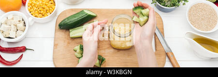 7/8-Ansicht von Frau hinzufügen gehackte Gurke in Glas Glas auf Holz Schneidebrett, Couscous, Panorama-Aufnahme ein. Stockfoto
