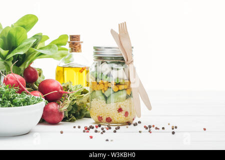 Frisches Gemüse Salat im Glas in der Nähe von Öl, Rettich und Gewürze isoliert auf weißem Stockfoto