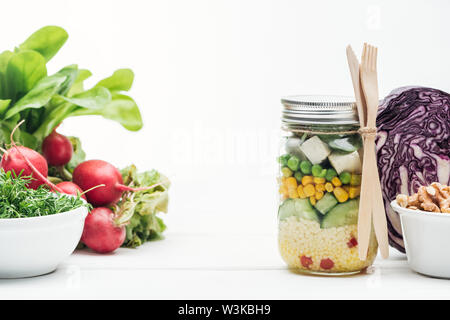 Frisches Gemüse Salat im Glas in der Nähe von Rettich, Rotkohl und Muttern isoliert auf weißem Stockfoto