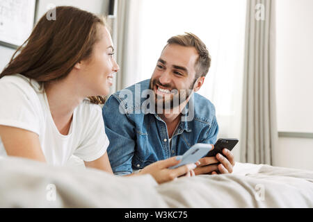 Schöne junge Paar in Liebe zu Hause, im Bett, über Mobiltelefone Stockfoto