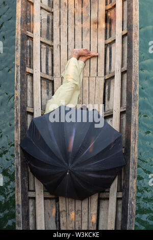 Die burmesische Mann schlafen in einem Boot mit schwarzem Dach am Inle See, Myanmar abgedeckt. Vertikale Ausrichtung. Stockfoto