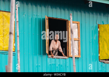 Maing Thauk, Myanmar - April 2019: alte Burmesische Frau mit Blick auf die schwimmende Haus Fenster. Stockfoto